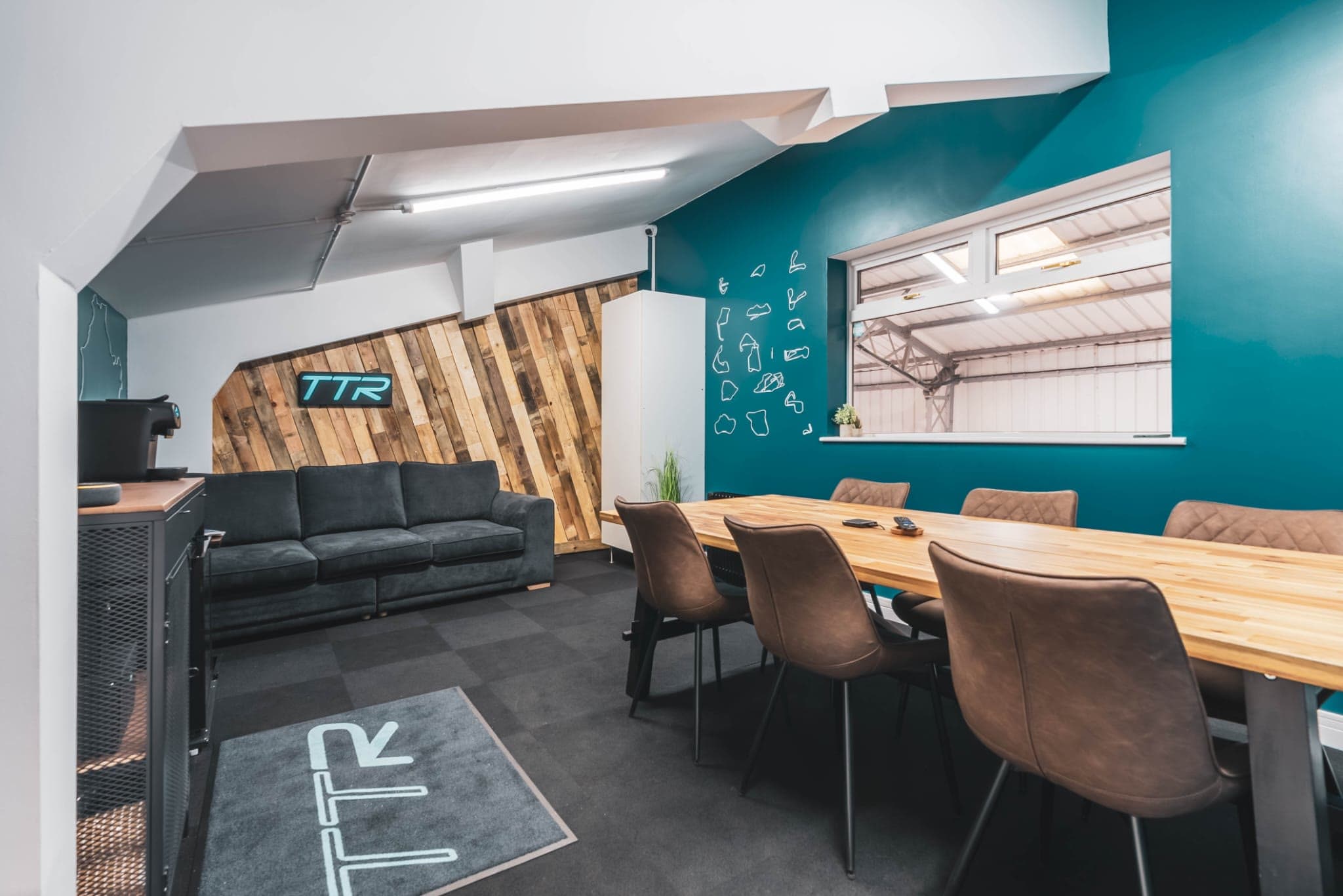 The TTR customer suite upstairs: the TTR logo on a reclaimed-timber wall, a sofa, the table and the TTR mat