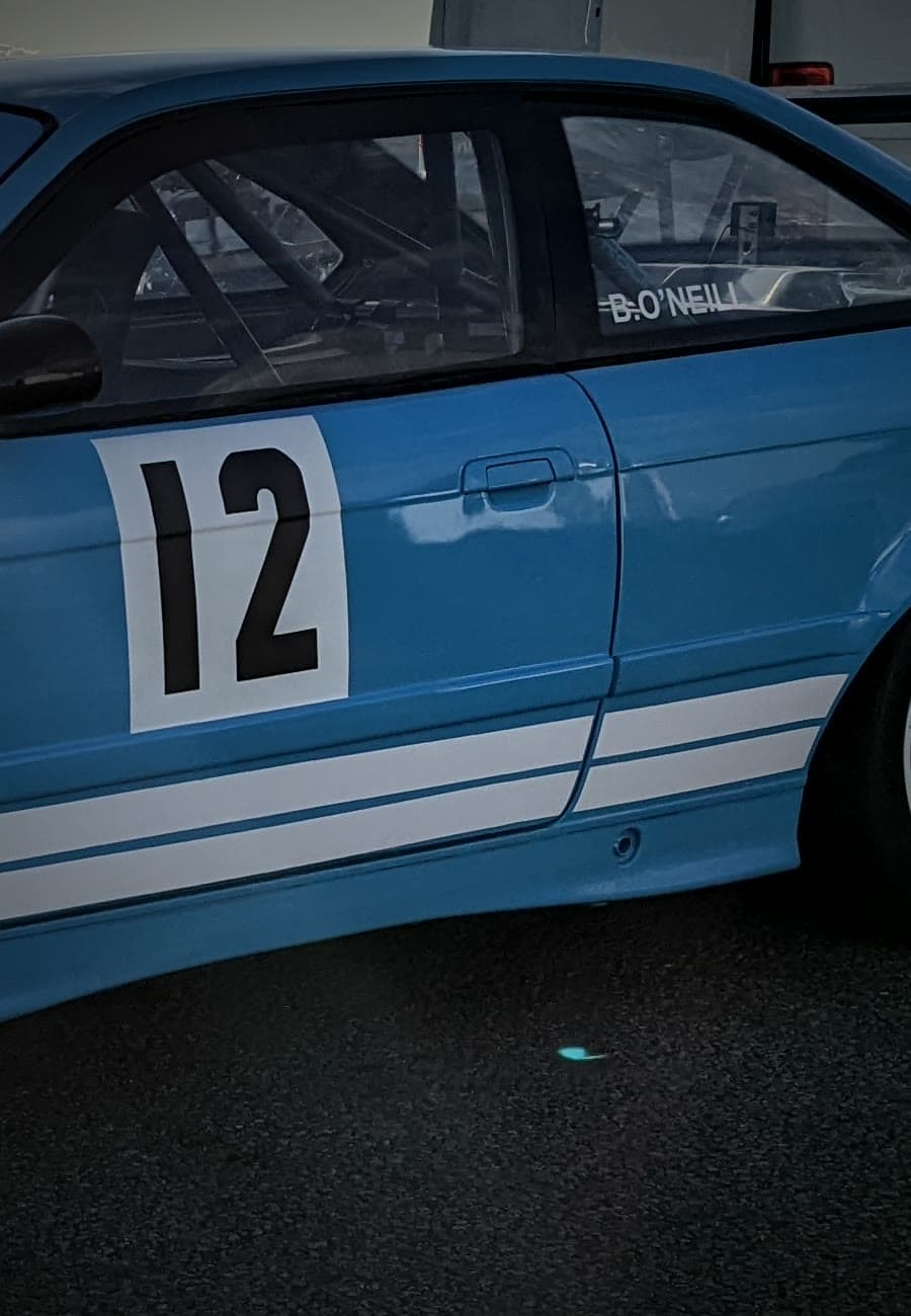 The light blue BMW E36 race car, number 12, in the paddock